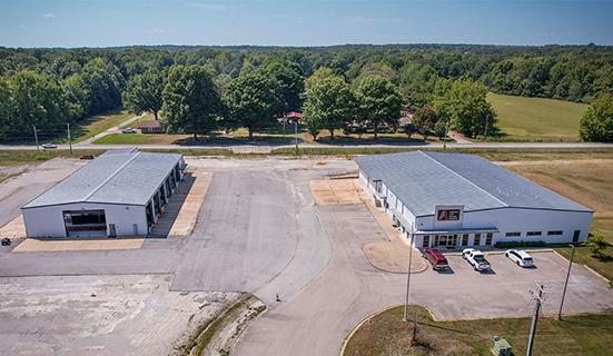 A building on left that is a 9,879 square foot shop and another building on the right that is a former dealership with offices and showroom that is 15,000 square feet located on 21.79 acres of land in Jonesboro, Arkansas at 5511 South Stadium Boulevard